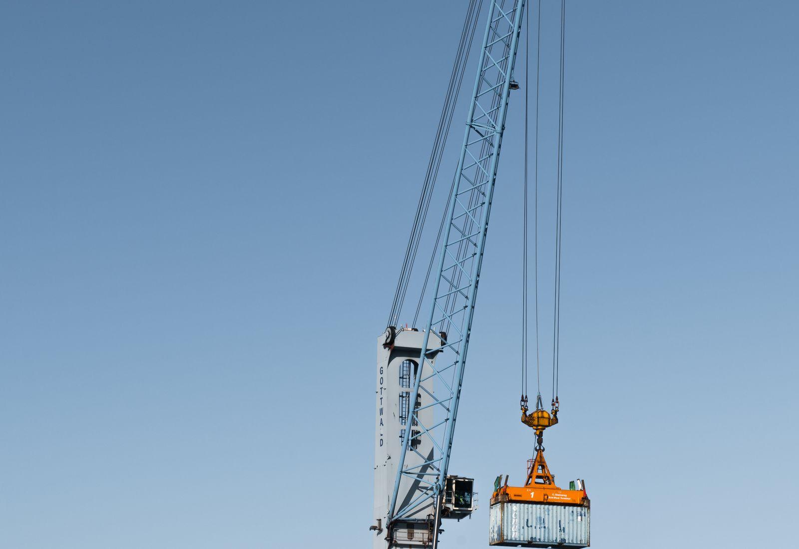 An industrial port crane lifting heavy cargo at a quayside under a clear sky (project cargo).